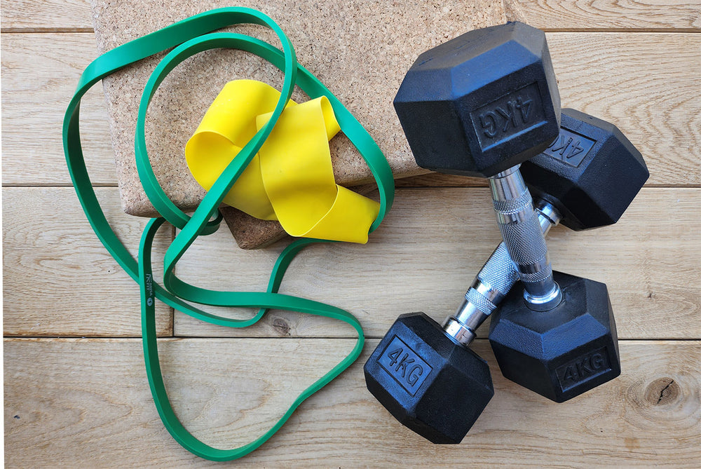 Pair of black dumbbells with green and yellow resistance bands on a wooden surface.