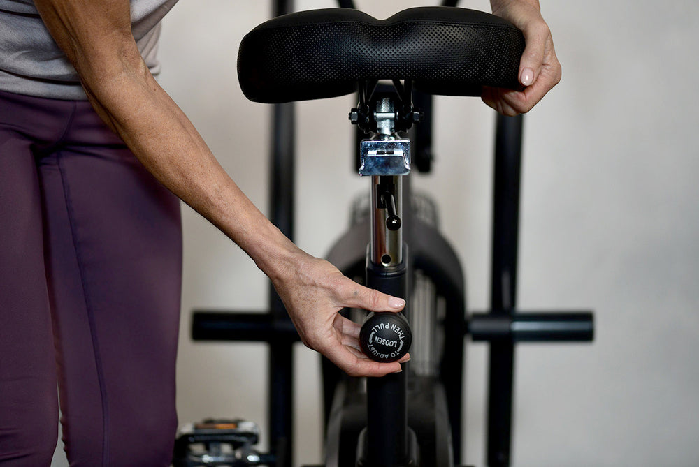 Person adjusting the seat position on a JTX Mission Air bike.