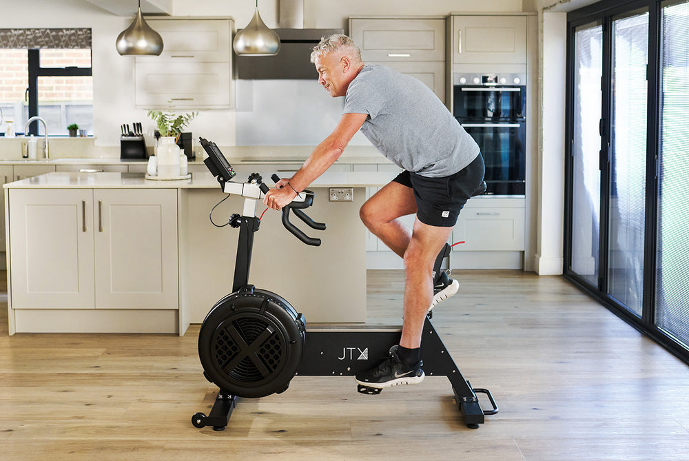 Man exercising on a JTX Ignite AirX Rider fan bike in a modern kitchen.