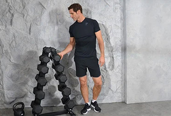 Man in a black t-shirt picking up a dumbbell from a dumbbell rack.