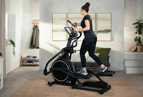 Woman exercising on a large black cross trainer in their living room.