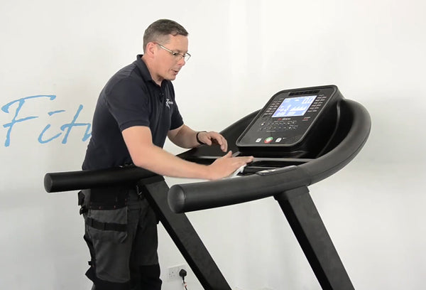Man wiping down the surface of a treadmill with a white wall background.