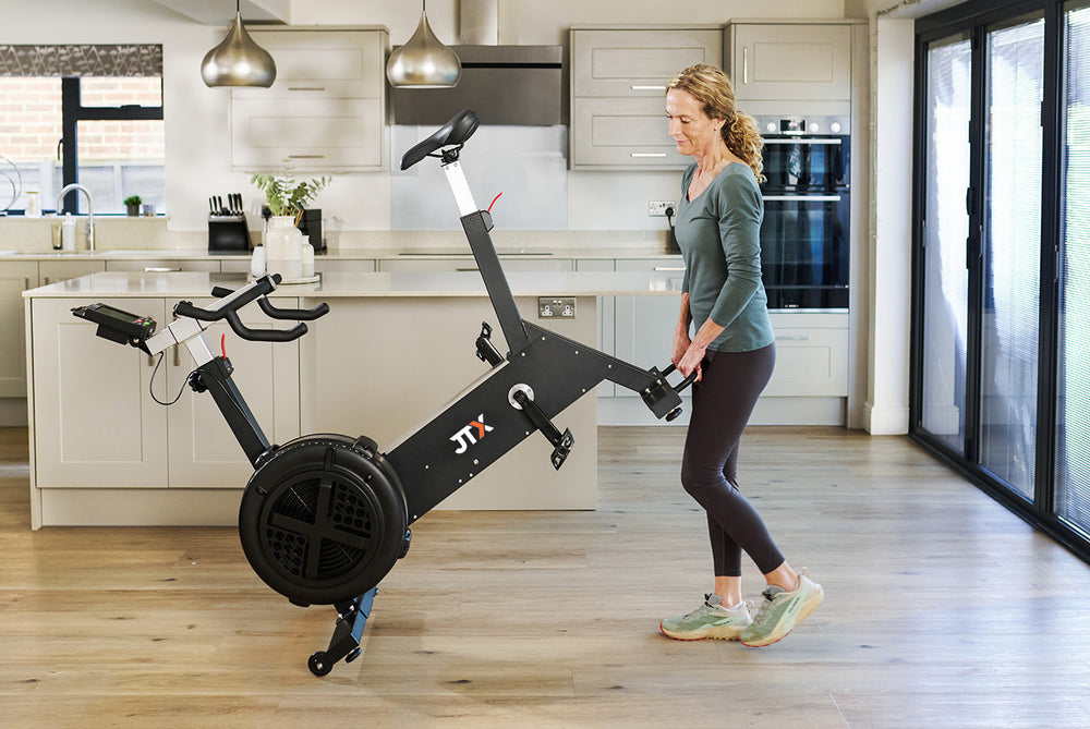 Woman moving the JTX Ignite AirX Rider exercise bike in their kitchen.