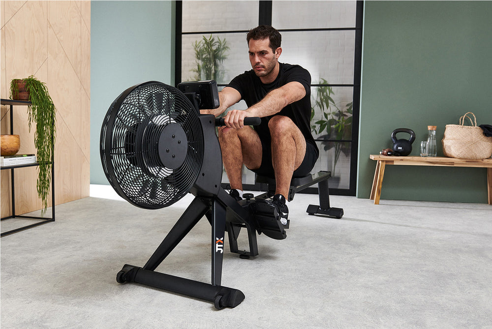 Front-on shot of a man using a JTX Freedom Air rowing machine in their living room.