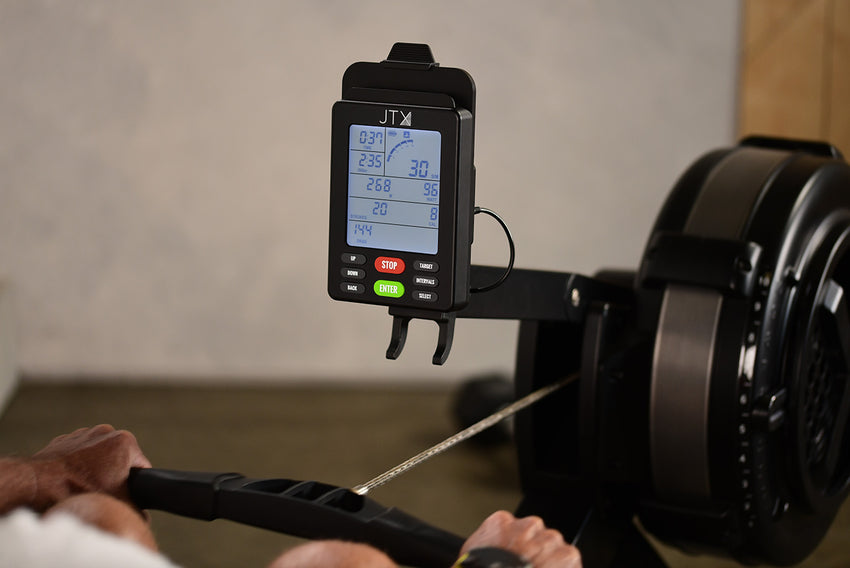 Person using a rowing machine with a close-up of the digital display showing workout metrics.