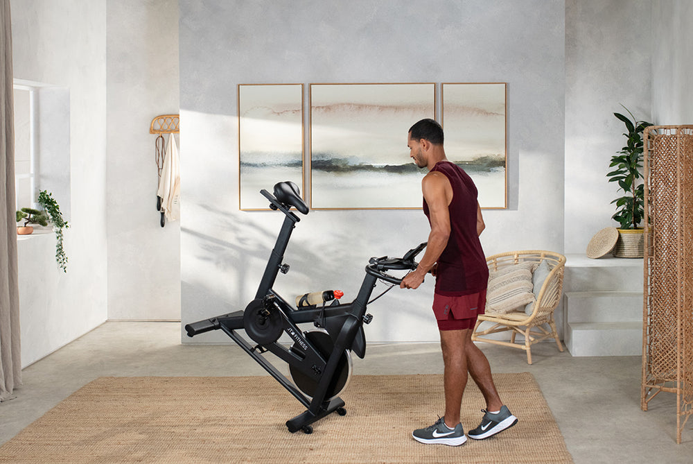 Man wheeling a JTX Cyclo-3M exercise bike through their living room.