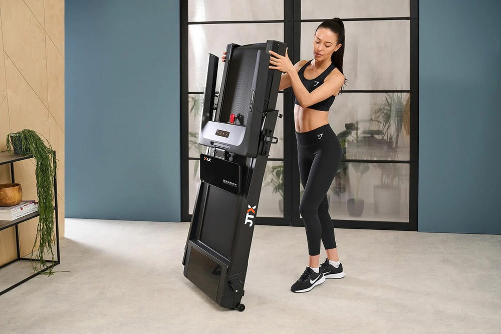 Woman folding up a JTX SlimLine treadmill and storing it upright in their home.