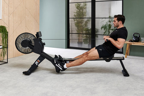 Man using a JTX Freedom Air mag-air rowing machine in their living room. His legs are fully extended as he performs a pulling motion.