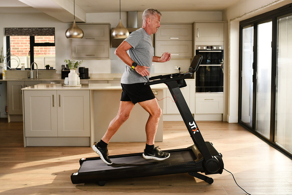 Man running at an incline on a JTX RunRise treadmill in a home setting.