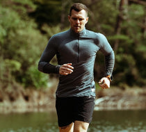 Man running outdoors with a lake and trees in the background.