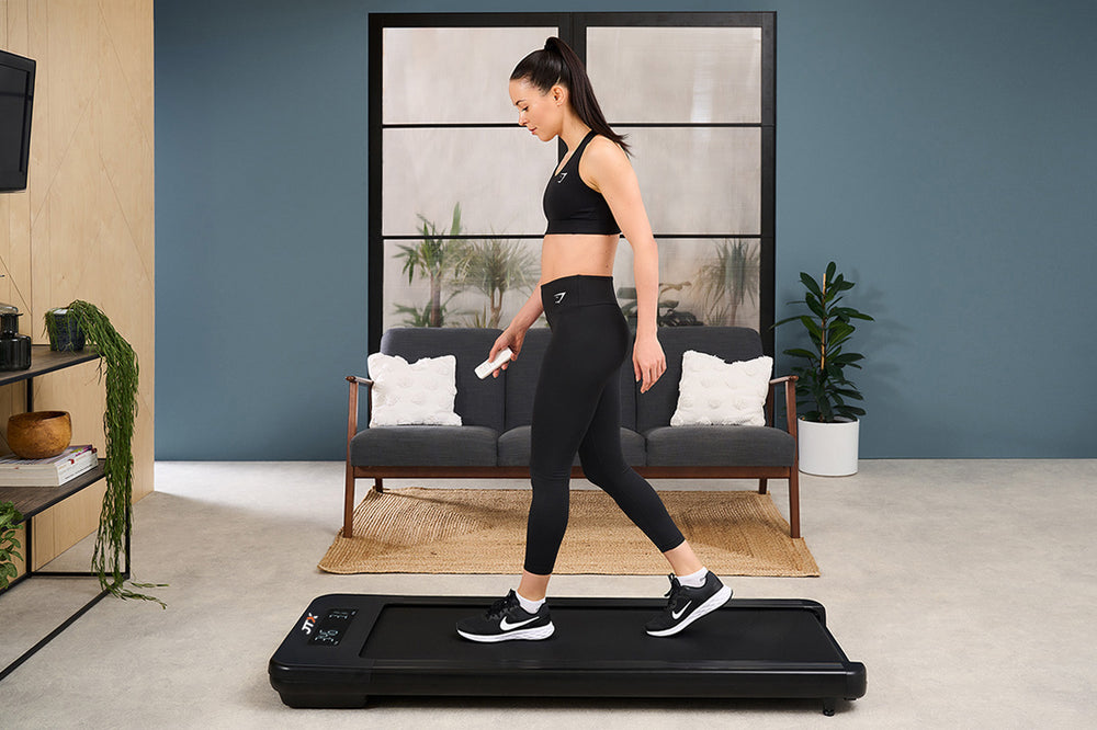 Woman walking on a JTX MoveLight walking pad while using the remote control to adjust speed.