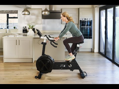 Woman exercising on a JTX Ignite AirX Rider fan bike in a kitchen.