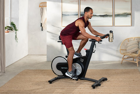 Man riding a JTX Racer-M exercise bike in their living room.