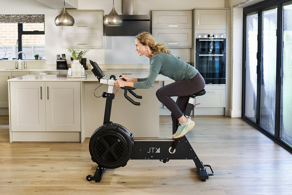 Woman riding a JTX Ignite AirX Rider fan bike in a modern kitchen.