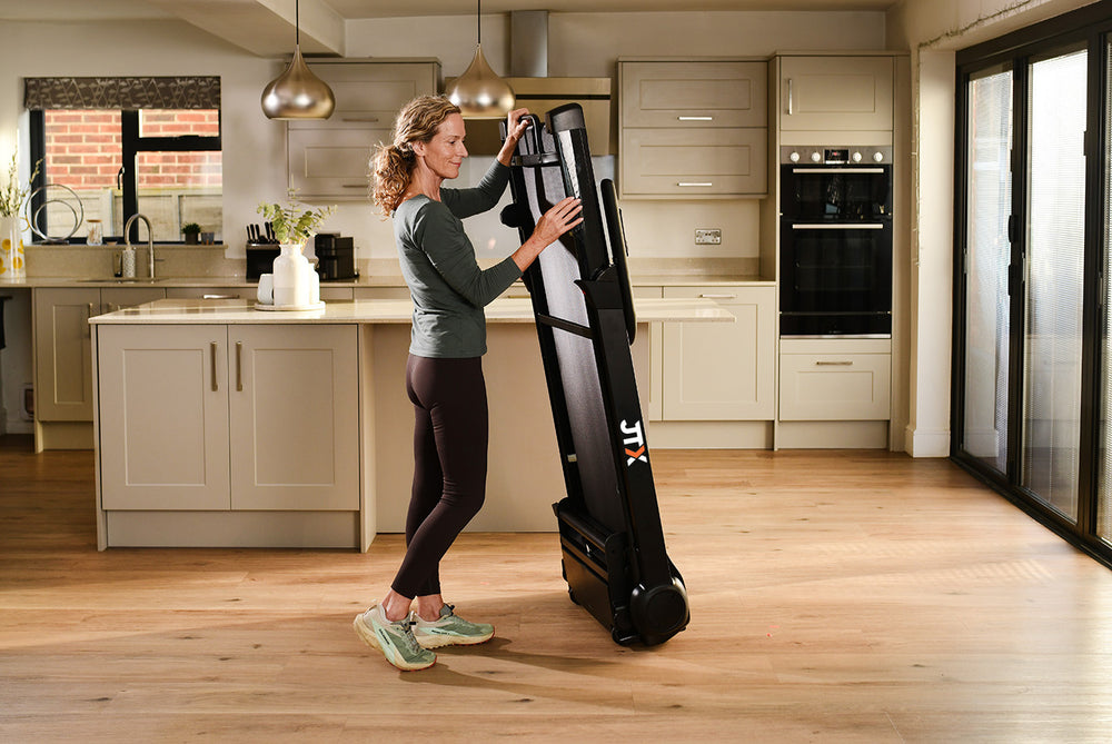 Woman holding a folded treadmill on its transport wheels.