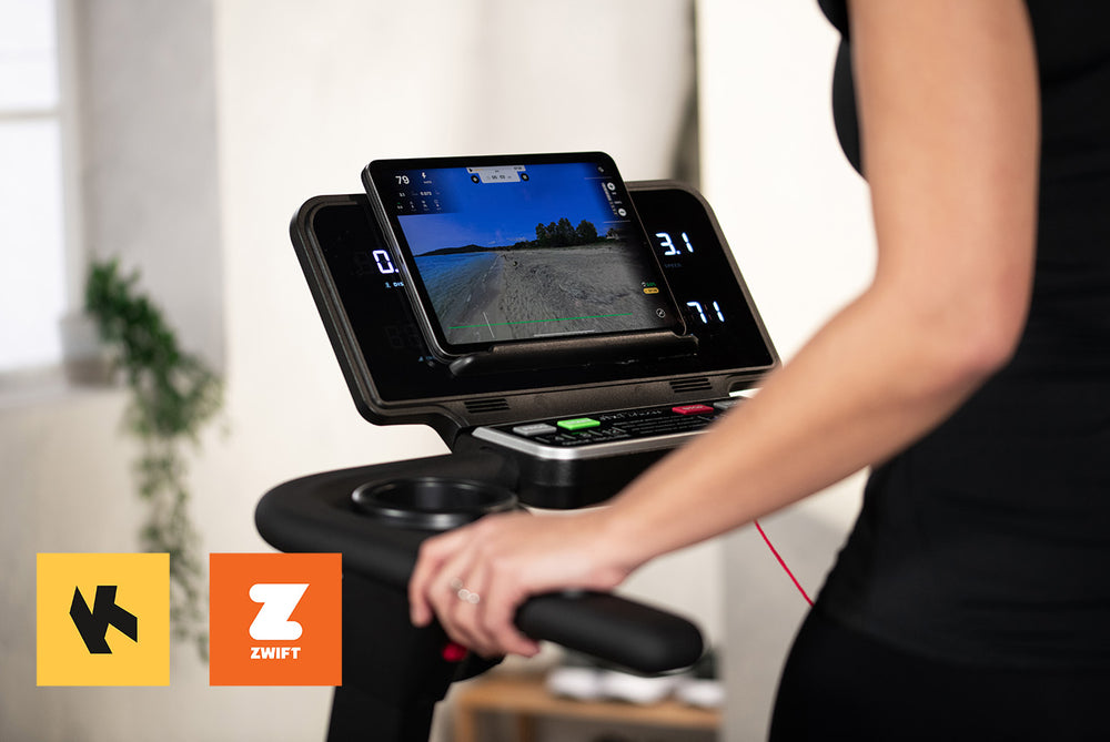 Person on a treadmill following a Kinomap route on their tablet. Kinomap and Zwift logos are on display.