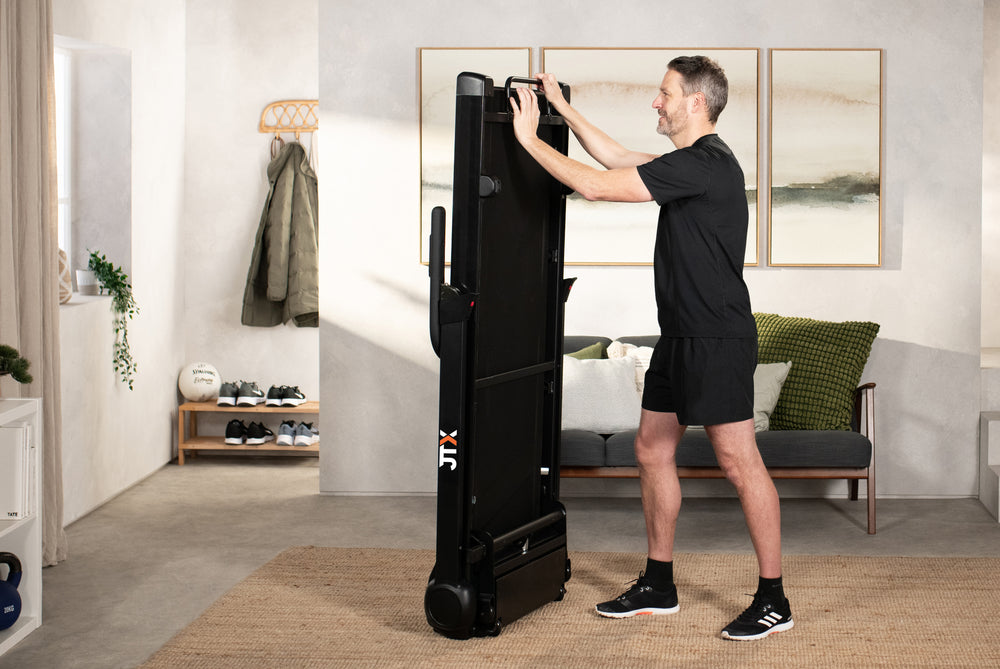 Man folding up a JTX RunRise Xl treadmill and storing it upright in their living room.