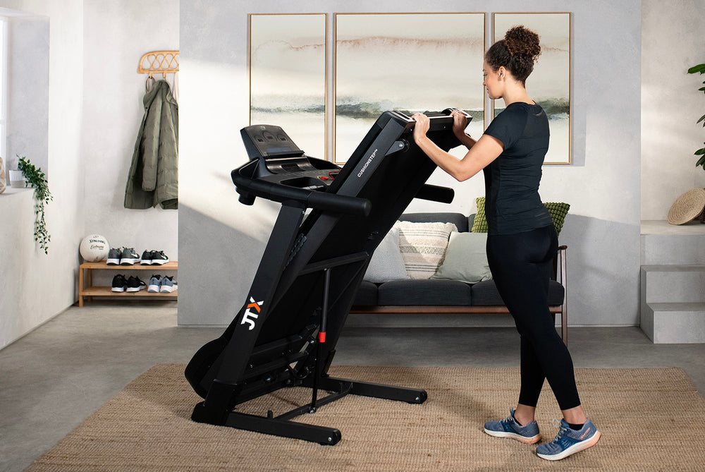 Woman folding up the deck of a JTX Sprint-7 treadmill in their living room.