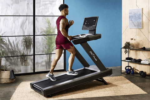 Man running at an incline on a JTX Sprint-9 Pro silver and black treadmill in a home setting.