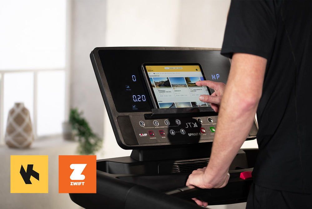 Man using a treadmill console with a tablet placed in the device holder. Zwift and Kinomap logos are on display.