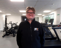 Man wearing a black jacket with JTX branding in a gym setting.