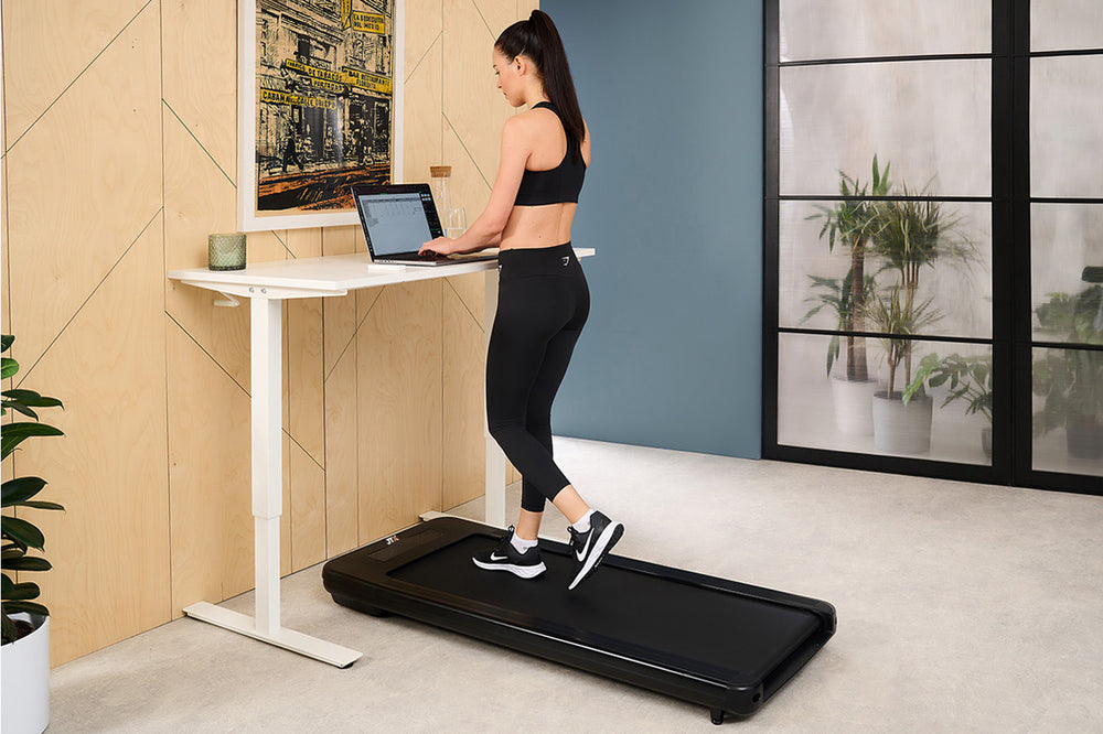 Woman using a laptop on a standing desk while walking on a JTX MoveLight walking pad.